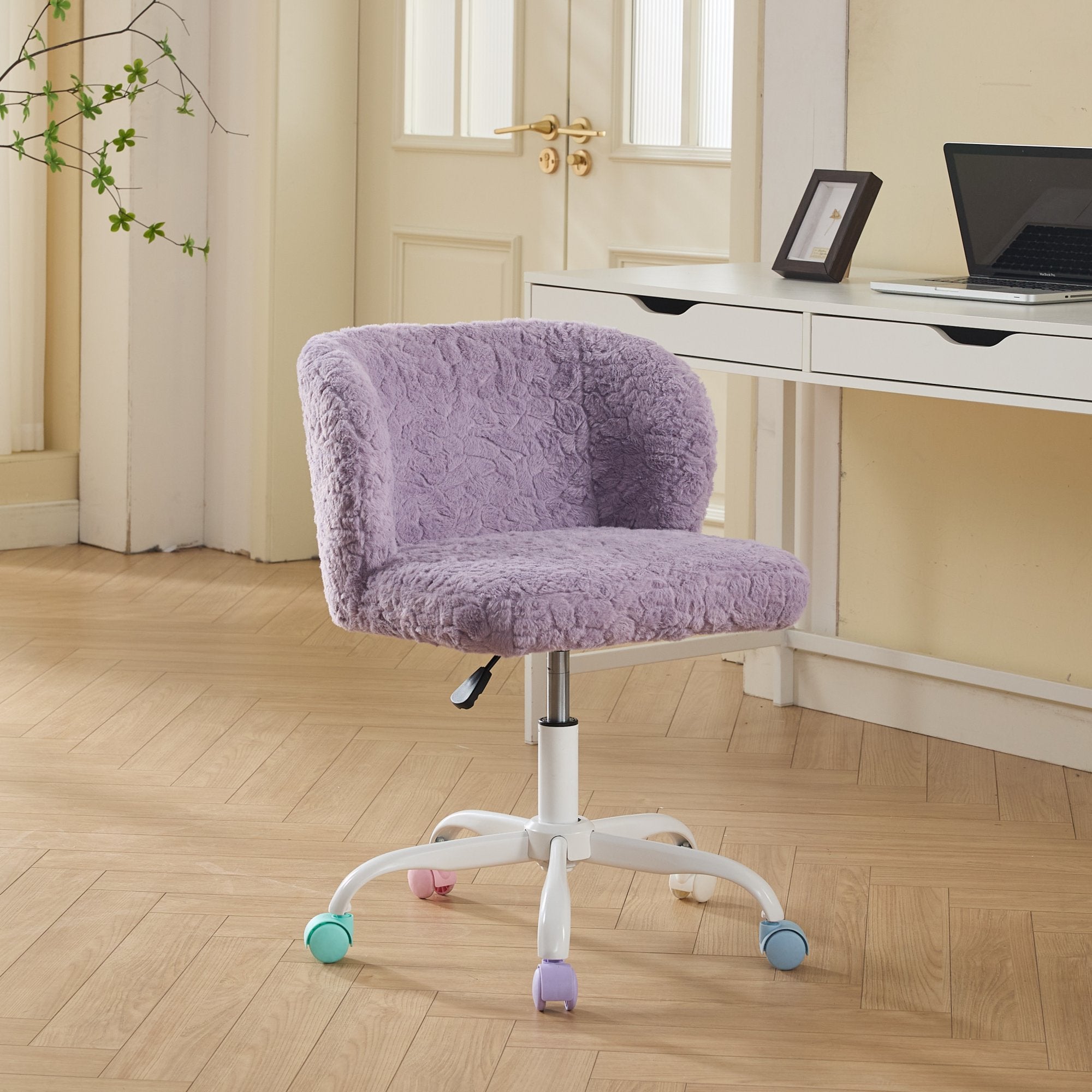 Violet ergonomic office chair with plush faux fur upholstery and multicolored caster wheels positioned in front of a white desk with a laptop and photo frame.