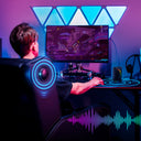 Person seated in an ergonomic gaming recliner chair with glowing speaker effects, using a computer in a colorful room with LED lights, showcasing office and game furniture.