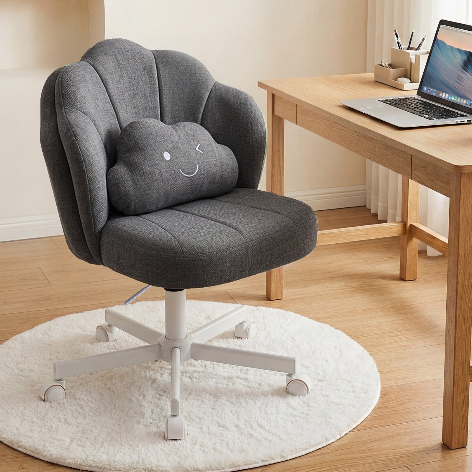 Gray ergonomic office chair with a curved petal design and a smiling cloud cushion, placed on a white rug next to a wooden desk with a laptop, styled for a home office.