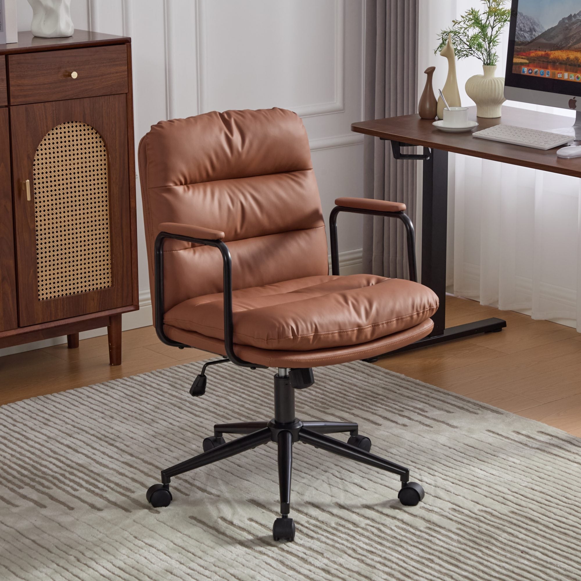 Brown ergonomic office chair with padded armrests and wheels on a black swivel base, positioned on a patterned rug in a modern home office setting.