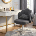 Dark gray petal-shaped vanity chair with white adjustable base and wheels, placed in a bright room next to a white and gold makeup vanity with beauty products, in a cozy home setting.