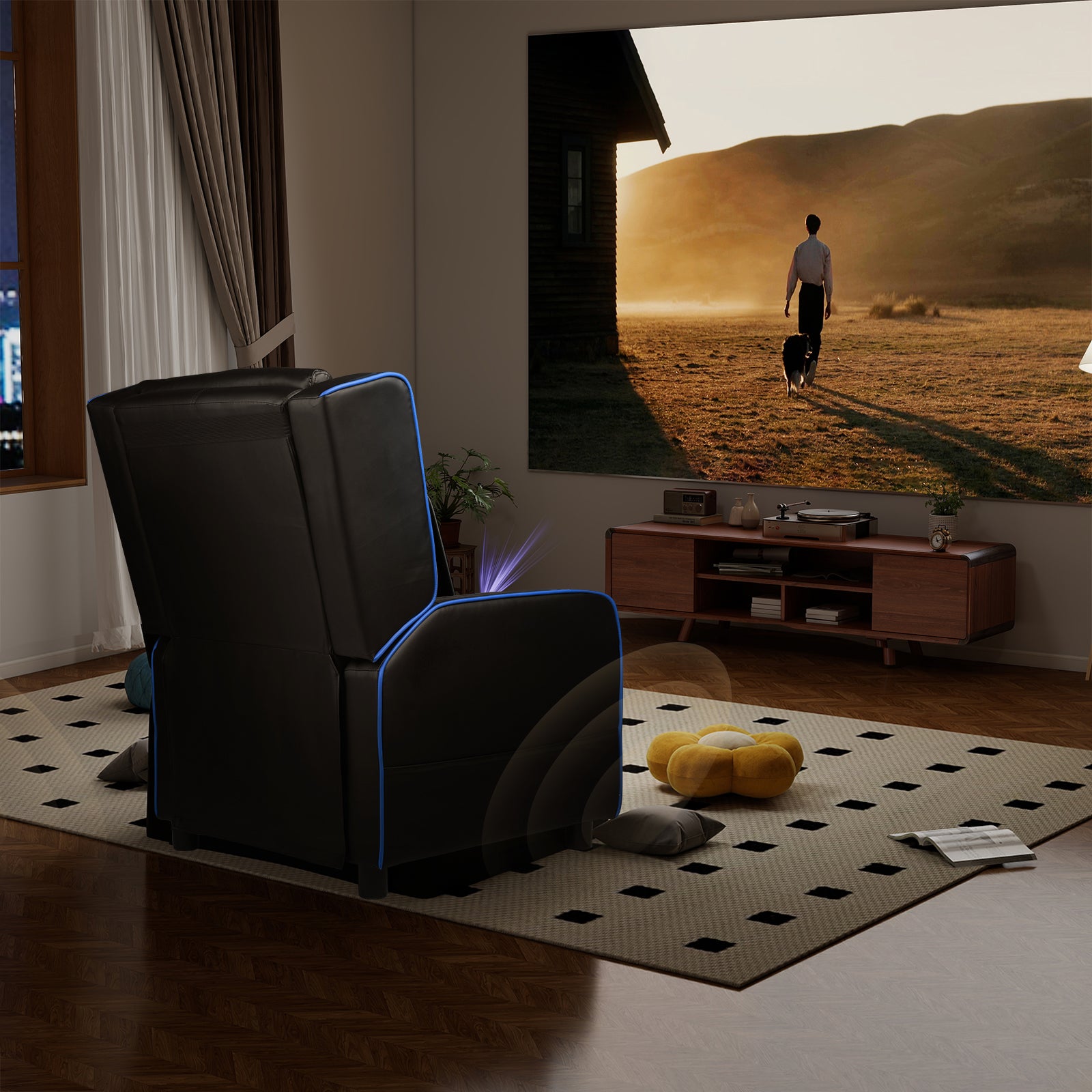 Black ergonomic recliner chair with blue LED accents positioned in a modern living room with a large projected screen, wooden cabinet, and patterned rug in an office and game furniture setting.