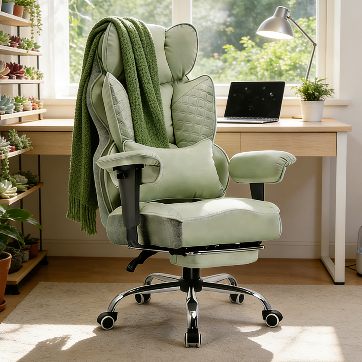 Green ergonomic office chair with quilted leather upholstery, adjustable armrests, footrest, and a matching green blanket draped over the back, placed in a bright home office with plants, a desk lamp, and a laptop on the desk behind it.