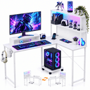 A white L-shaped gaming desk setup shown on a clean white background, with a computer monitor, keyboard, mouse, headset, shelving, plants, figurines, and a PC tower. The desk includes built-in cup holders and a wheeled base under the PC.