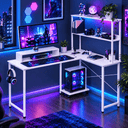 A modern white L-shaped gaming desk setup in a dark room with blue and purple ambient lighting. The desk includes a desktop monitor, keyboard, mouse, headset hanging on the left leg, a small RGB PC tower under the shelf, shelving with figurines and decor, and a computer mouse on top.