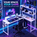 A white L-shaped gaming desk setup in a blue-lit room, featuring a computer monitor, keyboard, mouse pad, shelving unit, office chair, and PC tower. Promotional text at the top reads 'YOUR SPACE.