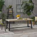 Wood outdoor patio table with grey wood top and black metal legs on stone patio, surrounded by garden plants and chairs with colorful cushions from Garden & Outdoor furniture collection.
